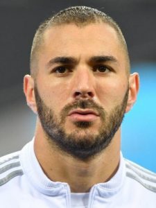 Twarz ogolonego na krótko Karima Benzemy w białym dresie z szarymi paskami na ramionach